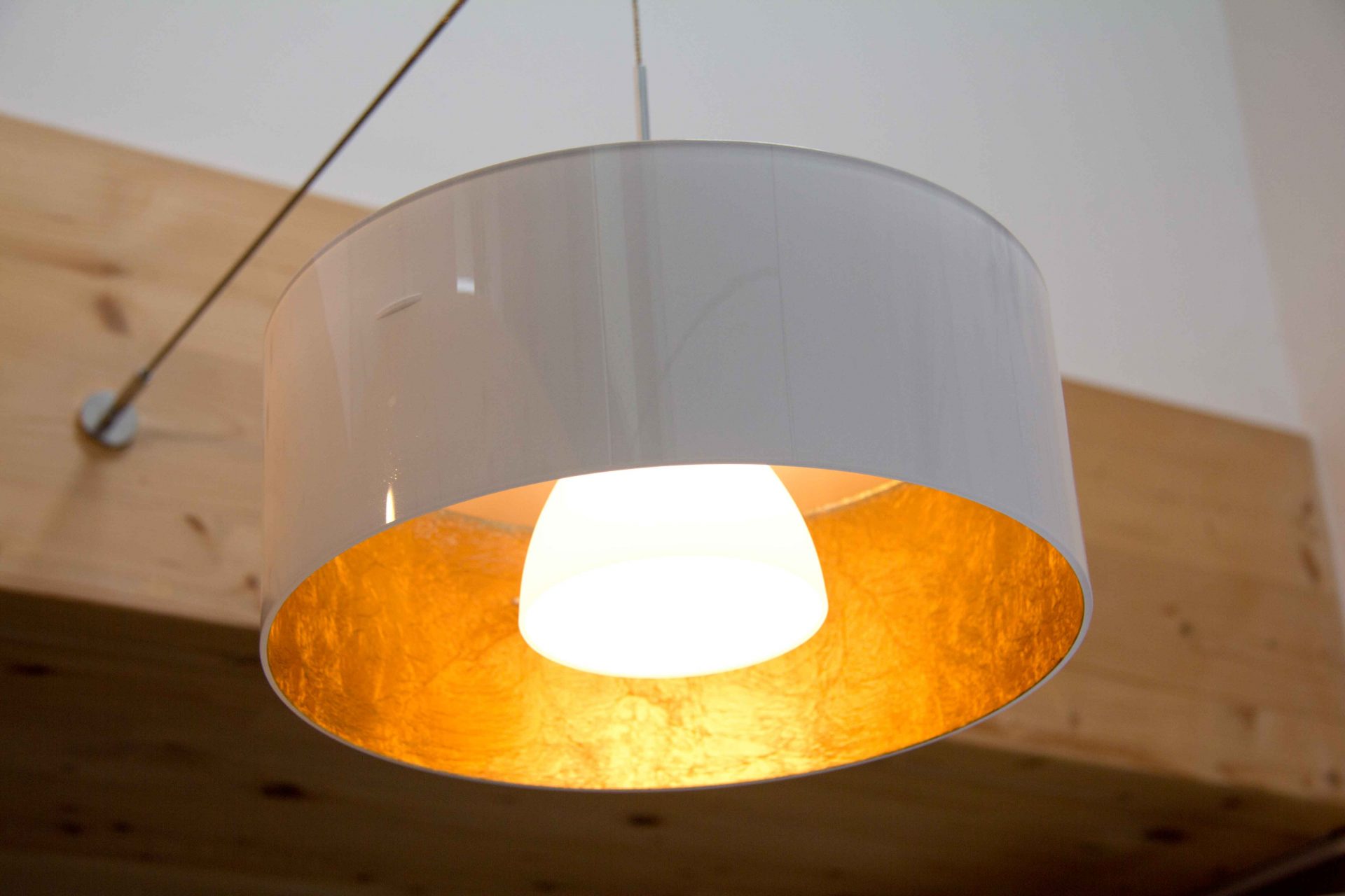 Moderne Esszimmer-Leuchte aus weißem Glas innen vergoldet. Sie strahlt ein sehr warmes Licht in der Farbe goldgelb nach unten ab.