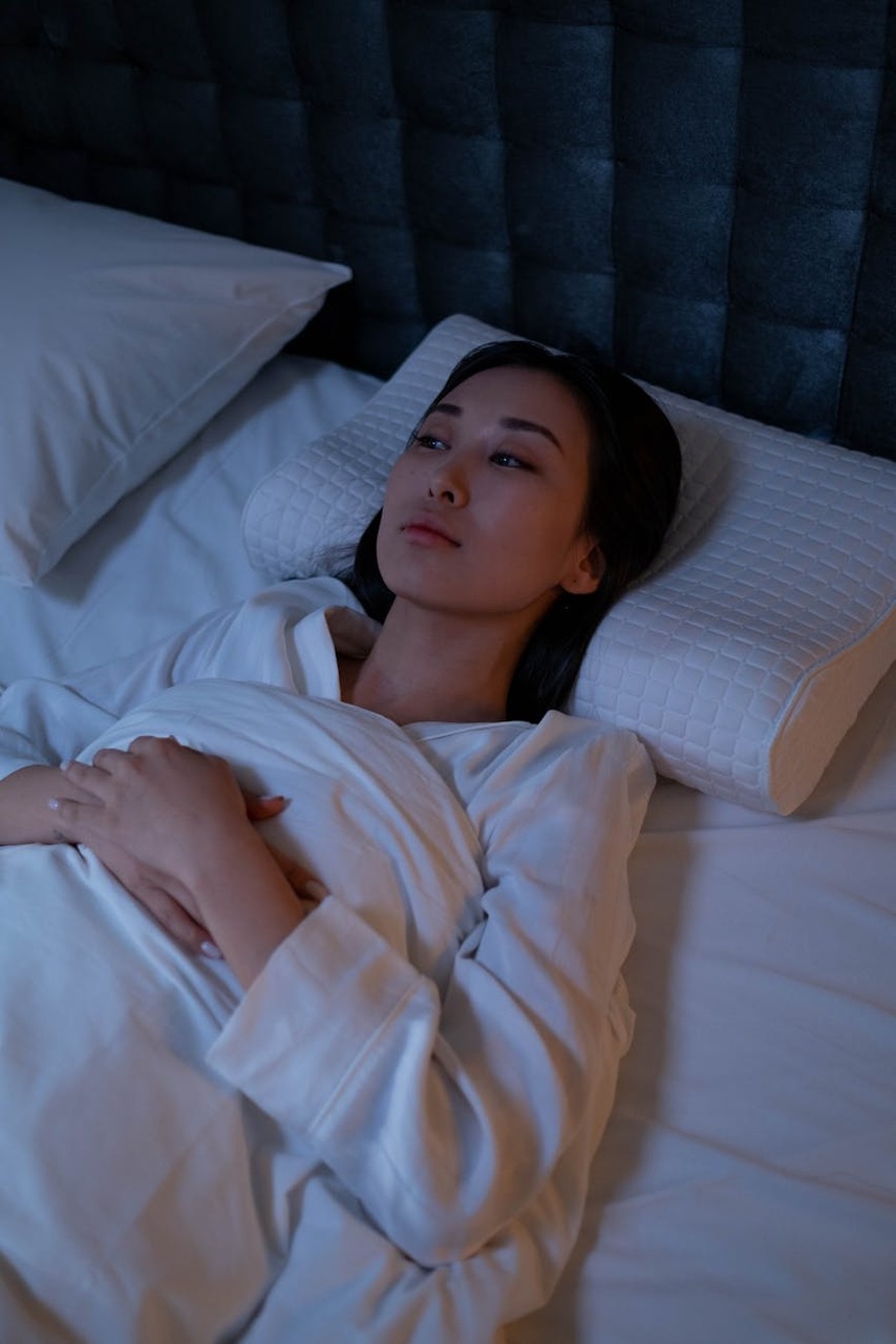 Eine Frau in weißem Pyjama liegt schlaflos im Bett.