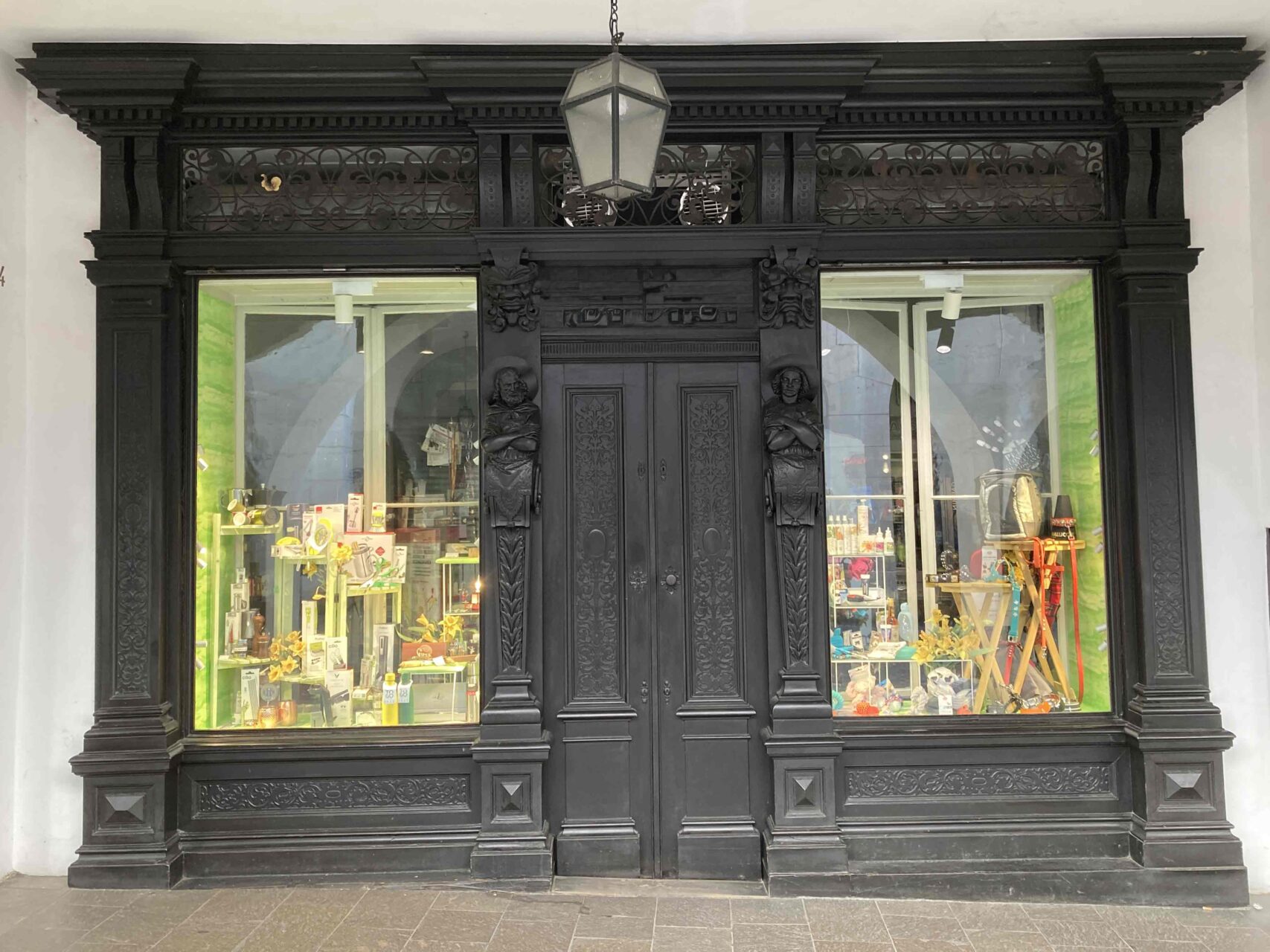 Beispiel für einen historischen Eingangsbereich mit einer schwarzen Türe. Links und rechts von der Türe befinden sich Schaufenster. Es handelt sich um ein Geschäft für Dekobedarf.